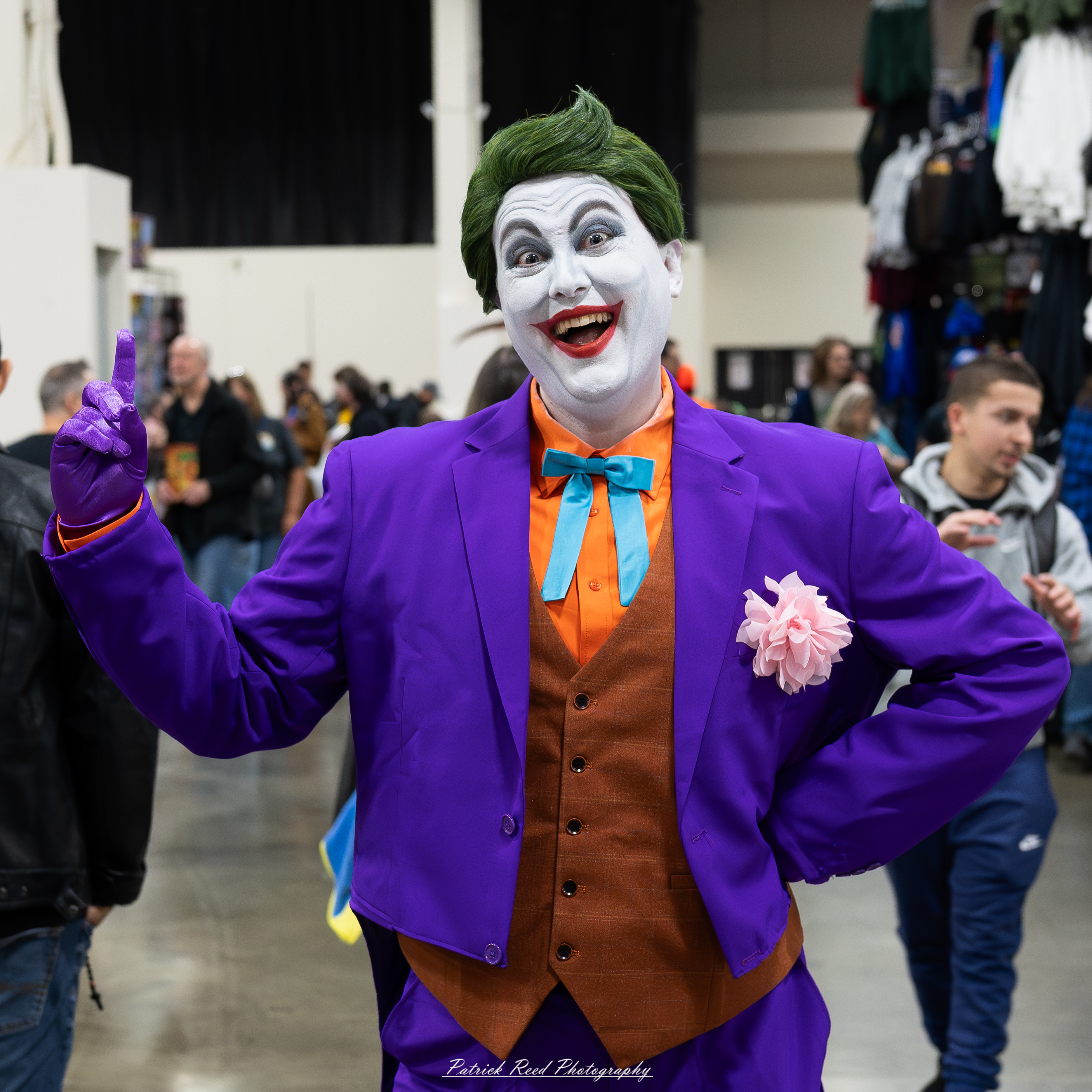 "Cosplayer dressed as the Joker, featuring the character's signature purple suit, green hair, and white face paint with a mischievous smile, capturing the iconic look of the chaotic villain from DC Comics."